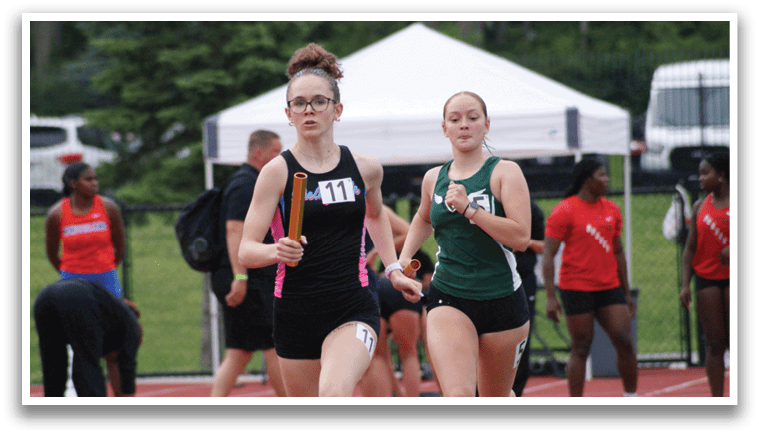 Three women are running on a track, with one wearing a green shirt and the other two wearing black. They are all running in the same direction, with one of the women in the lead. Contenido generado con IA