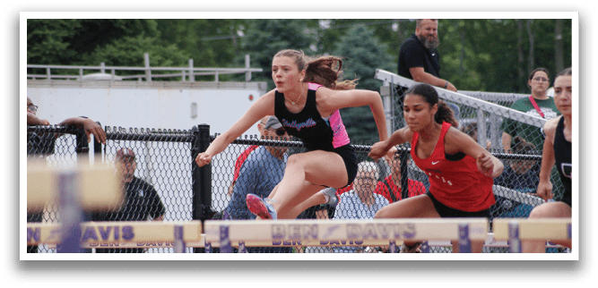 Two female athletes are running on a track, one of them jumping over a hurdle. Contenido generado con IA