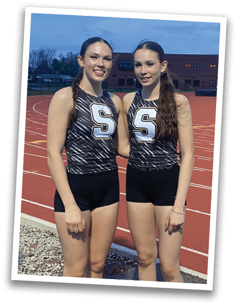 Two female runners in uniforms pose for a picture on a track. Contenido generado con IA