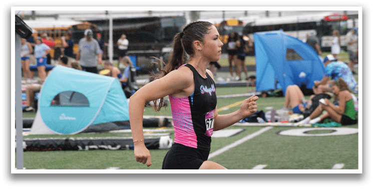 Three female runners are racing on a track, with one wearing a green shirt and the other two wearing red. Contenido generado con IA