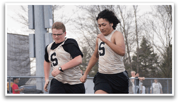 Two people running on a track, one wearing a black shirt and the other wearing a gold shirt. Contenido generado con IA