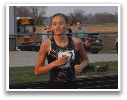 A woman is running on a track, wearing a black shirt and white shoes. She is in the lead and appears to be focused on her race. There are several other people in the background, some of whom are also running. A car is parked in the background, and a truck is visible further back. Contenido generado con IA