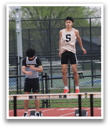 A man is jumping over a hurdle on a track, while another man watches. Contenido generado con IA