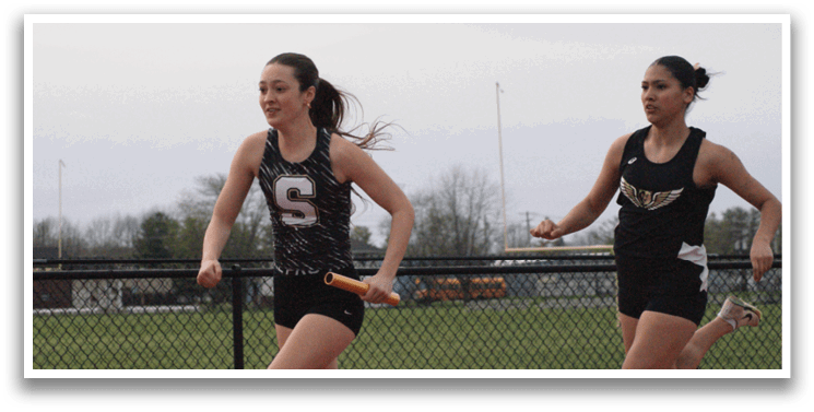Two female runners are on a track, one wearing a black and white outfit and the other wearing a black and white and gold outfit. They are running in opposite directions. Contenido generado con IA