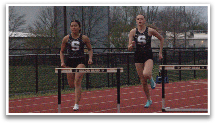 Three female athletes running on a track, one of them wearing a black shirt with the number 7. Contenido generado con IA