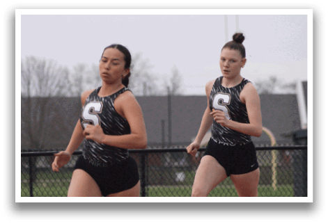 Two female runners are running on a track, one wearing a black and white outfit and the other wearing a black and white and black outfit. Contenido generado con IA