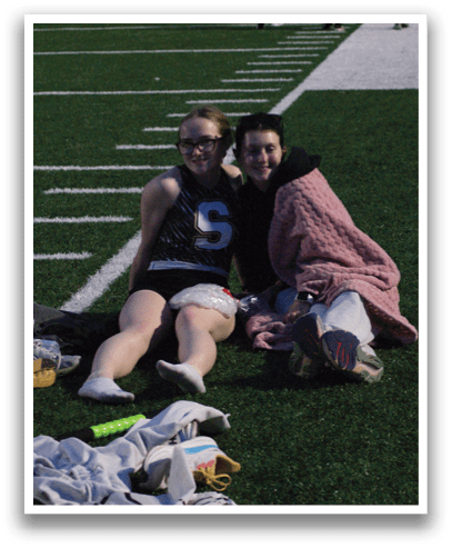 Two women are sitting on a football field, one of them is holding a blanket. Contenido generado con IA
