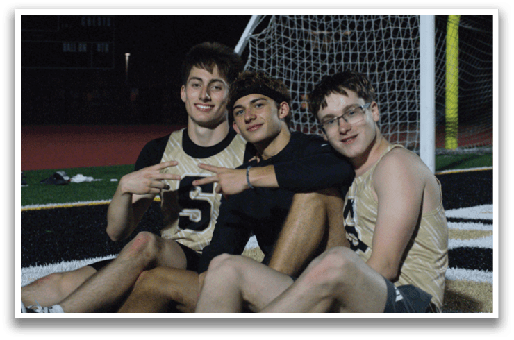 Three young men are sitting on the ground in front of a soccer goal. Contenido generado con IA