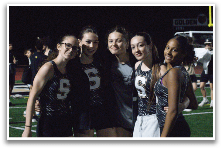 Four women pose for a photo on a field. Contenido generado con IA