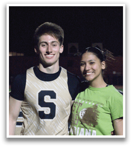 A man and woman are standing on a football field, posing for a picture. The man is wearing a football jersey with the number 6 on it. Contenido generado con IA