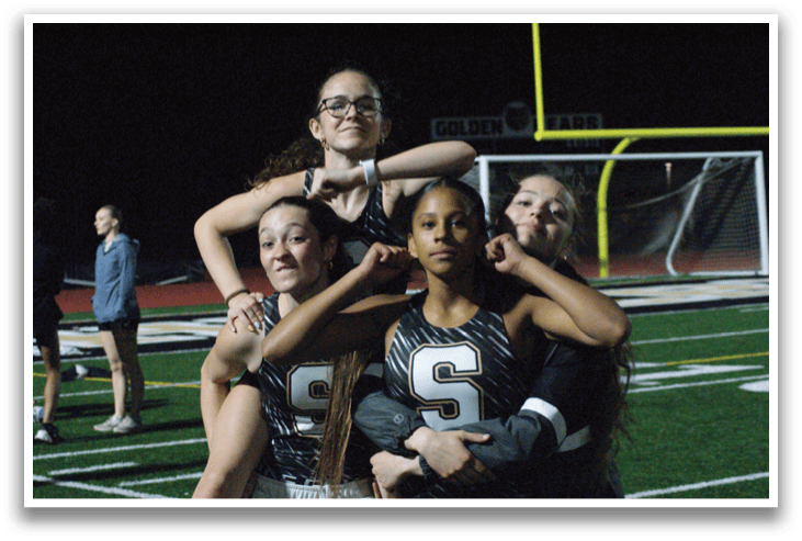 Four female athletes hugging each other on a field. Contenido generado con IA