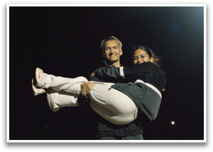 A man and woman are standing outside at night, the woman is holding the man in a bear hug. Contenido generado con IA