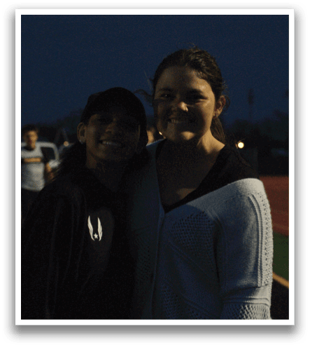 Two women standing on a track, one wearing a black hat. Contenido generado con IA