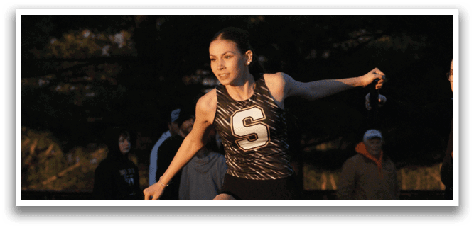 A female athlete in a black and white uniform is running on a track. Contenido generado con IA