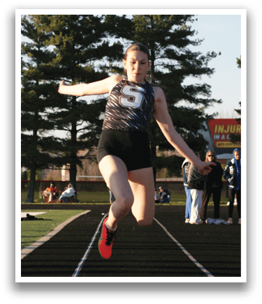 A woman is jumping in the air on a track, wearing a black and white shirt. Contenido generado con IA