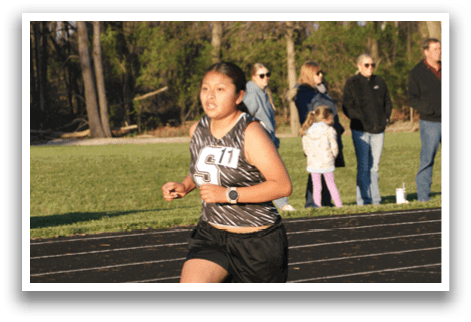 A woman is running on a track while wearing a number 61 shirt. Contenido generado con IA