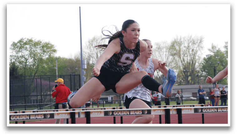 Two female athletes are competing in a pole vaulting event. One athlete is in the process of jumping over the bar, while the other is running behind her. Contenido generado con IA