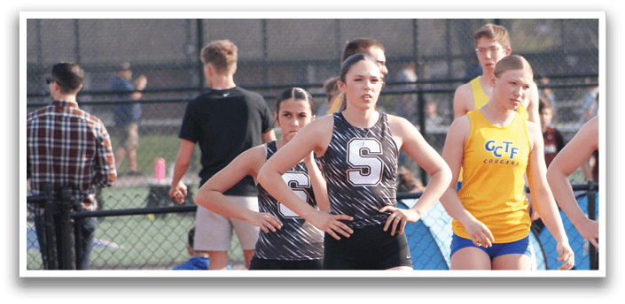 A group of female athletes are lined up on a track, preparing for a race. Contenido generado con IA