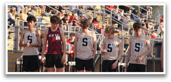 A group of young men are standing on a track, wearing uniforms and number tags. They are lined up, possibly for a race or competition. Contenido generado con IA