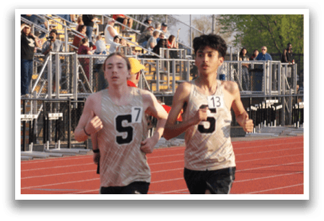 Two young men are running on a track, one wearing a white shirt and the other wearing a black shirt. They are both running towards the finish line. Contenido generado con IA