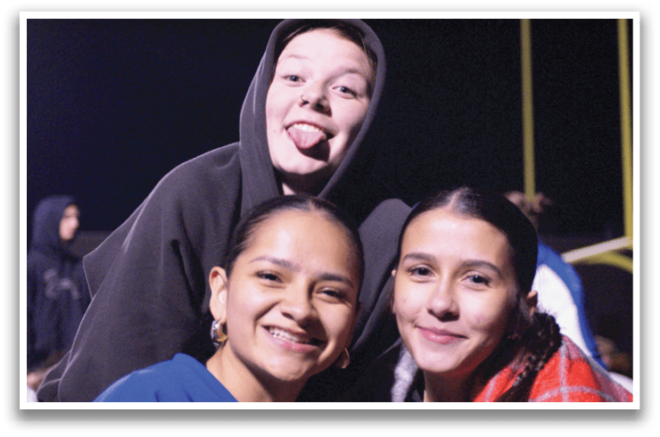 Three young people pose for a picture, with one of them sticking out her tongue. Contenido generado con IA