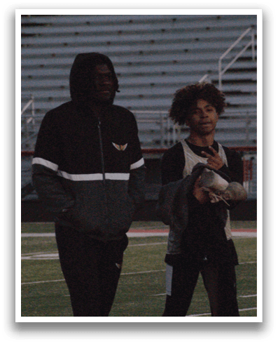 Three people standing on a field, two of them wearing black and white jackets. Contenido generado con IA