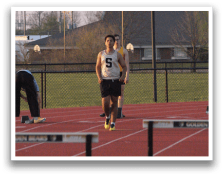 Three men are standing on a track, one of them is bending over. Contenido generado con IA