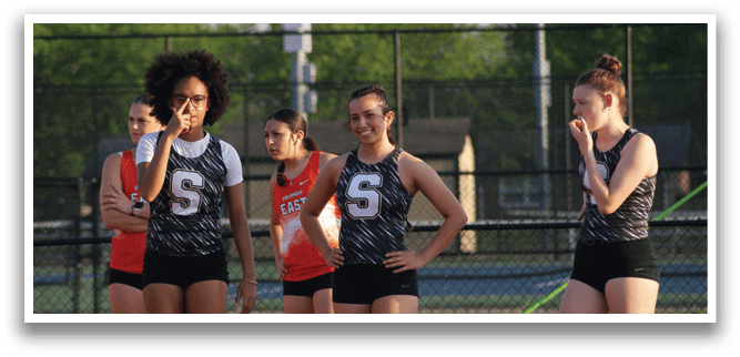 A group of female athletes are standing on a track, wearing uniforms and holding their hands on their hips. Contenido generado con IA