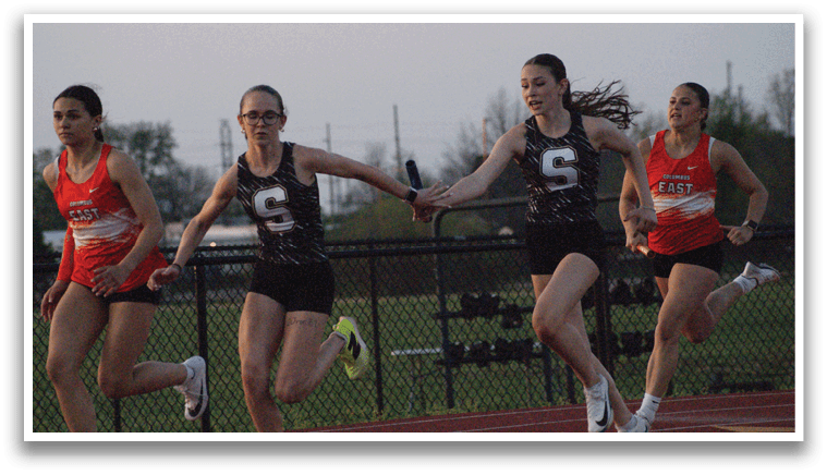 Three female runners are shown in a track competition. Two of them are wearing black and white uniforms, while the third one is wearing an orange and white uniform. They are running on a track, with one of them holding a baton. Contenido generado con IA