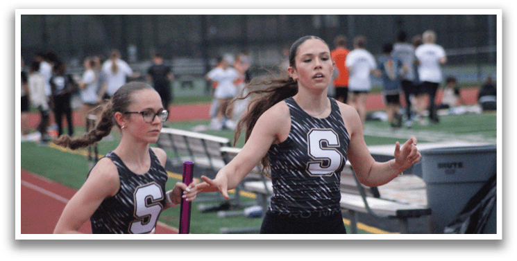 Two girls running on a track, one wearing a S shirt. Contenido generado con IA