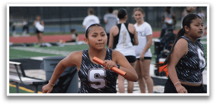 Two female athletes are running on a track, one with a bat and the other with a frisbee. Contenido generado con IA