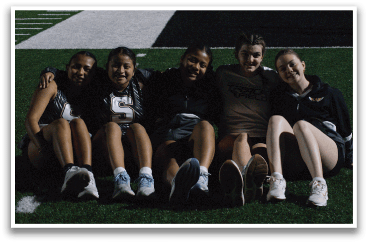 Five women are sitting on the grass, posing for a picture. Contenido generado con IA