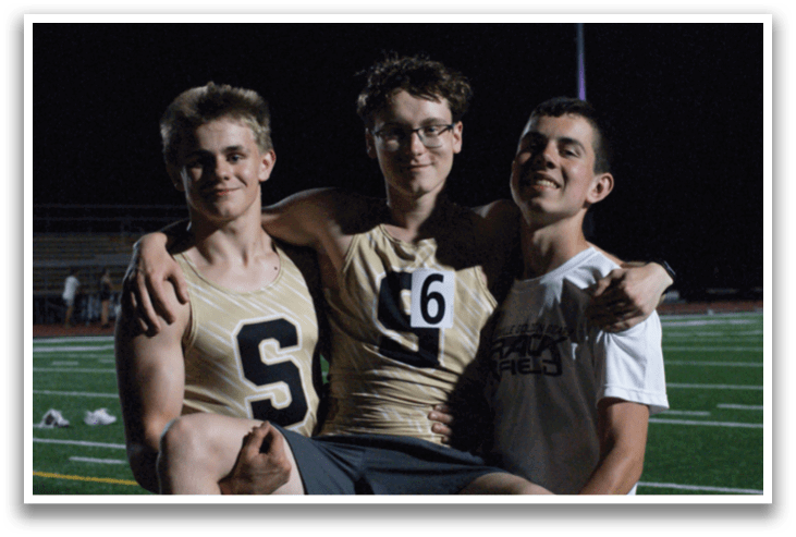 Three men are standing on a field, posing for a picture. One man is holding another man on his shoulders, and the third man is standing next to them. Contenido generado con IA