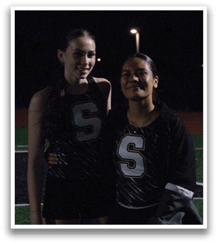 Two girls standing on a field, one is taller than the other. Contenido generado con IA