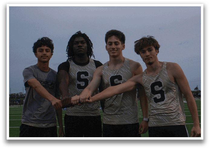 Five young men wearing black jackets and hoods stand on a field. Contenido generado con IA