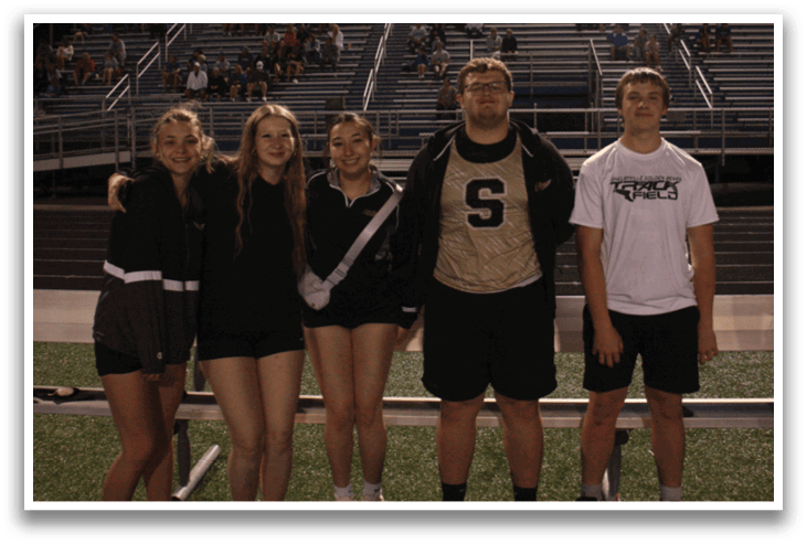 Five people pose for a photo on a field. Contenido generado con IA