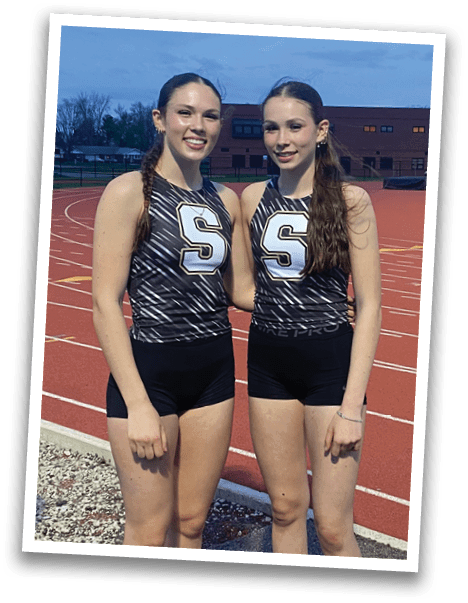 Two female runners in uniforms pose for a picture on a track. Contenido generado con IA