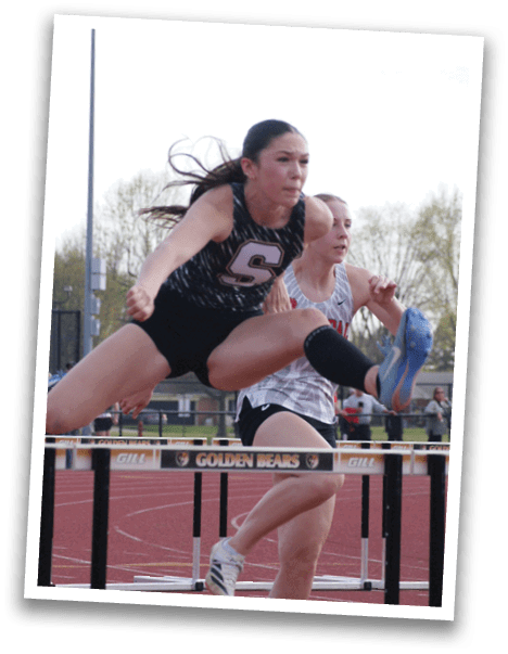 Two female athletes are running on a track, one jumping over a hurdle. Contenido generado con IA
