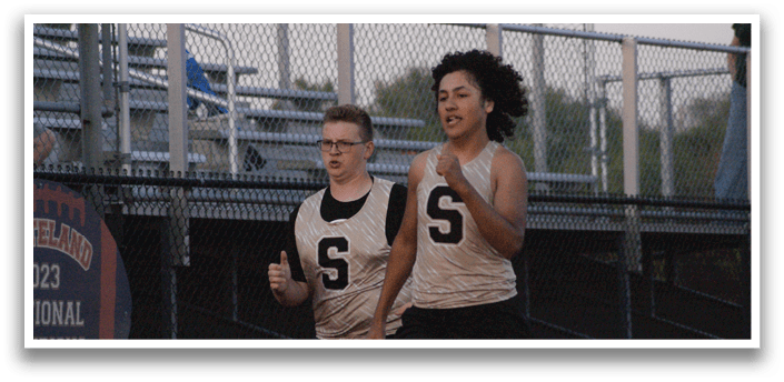 Two boys are running on a track, one wearing a white shirt with the letter S on it. Contenido generado con IA