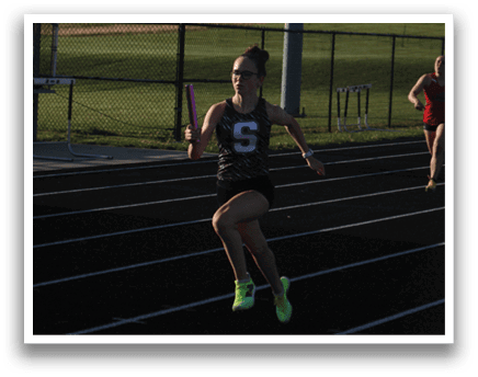 Two female runners are racing on a track, one wearing a red shirt and the other wearing a black shirt. They are both running with determination, with one of them holding a pink object in her hand. Contenido generado con IA