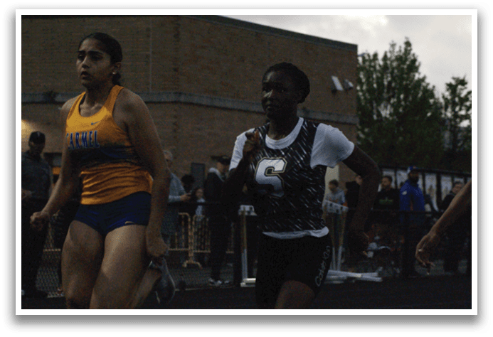Two female runners are racing on a track, one wearing a yellow and blue outfit and the other in a black and white outfit. They are running in front of a crowd of spectators. Contenido generado con IA