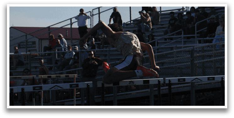 A man is jumping over a hurdle on a track, with several people watching from the stands. Contenido generado con IA