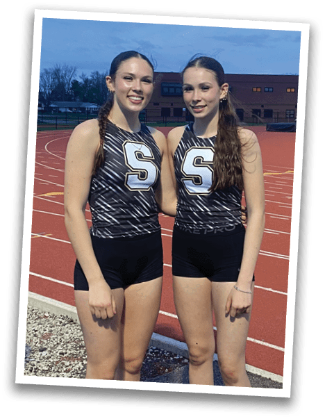 Two female runners in uniforms pose for a picture on a track. Contenido generado con IA
