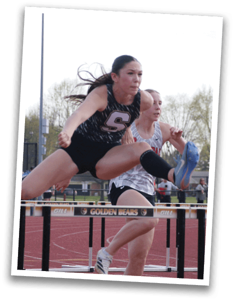 Two female athletes are running on a track, one jumping over a hurdle. Contenido generado con IA