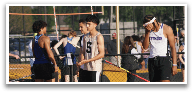 A group of people are standing on a track, some of them wearing uniforms. They are holding poles and appear to be participating in a track event. Contenido generado con IA