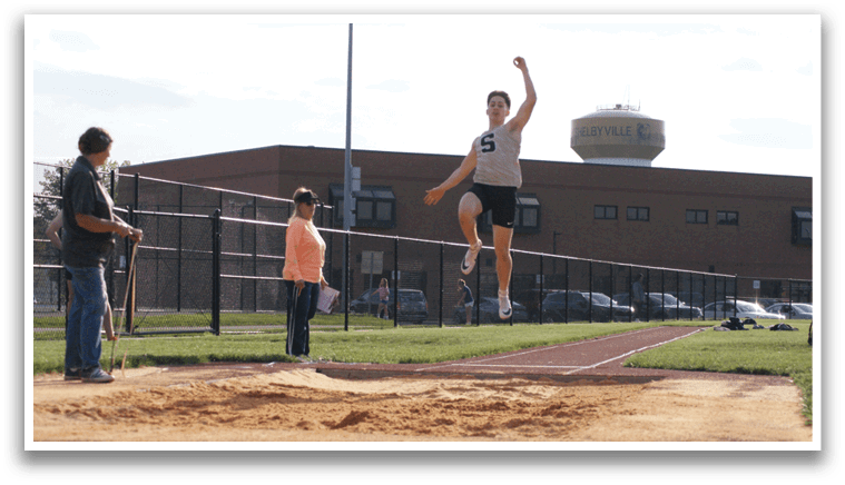 A man is jumping in the air over a hurdle, with a woman watching from behind. Contenido generado con IA