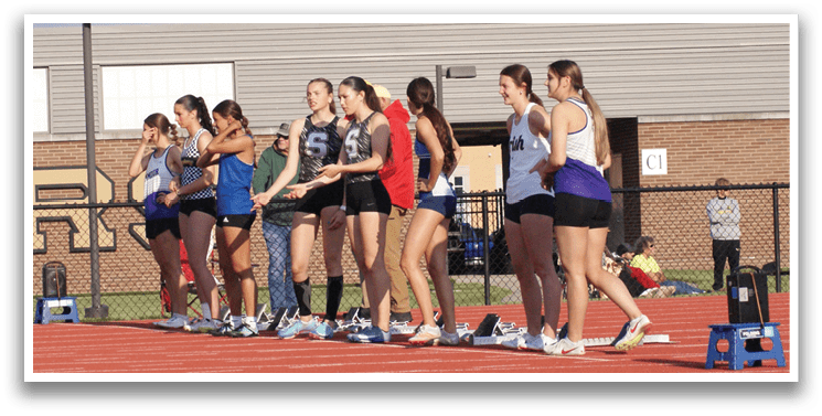 A group of female athletes are standing on a track, wearing uniforms and holding their hands up. Contenido generado con IA