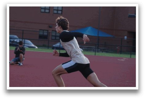 A man is running on a track, wearing a black and white shirt. Another person is sitting on the ground, watching the man run. Contenido generado con IA