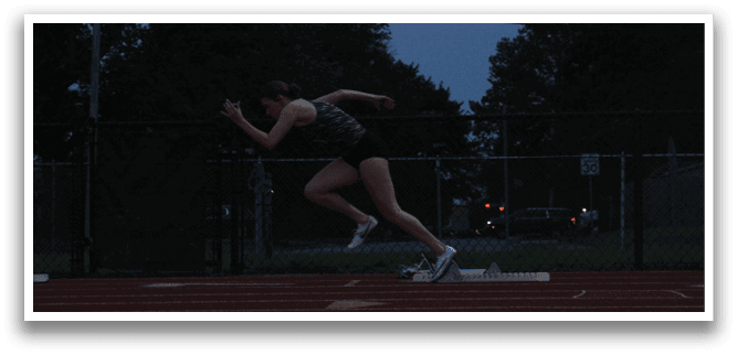 Two women are running on a track, one in the foreground and the other in the background. The woman in the foreground is wearing a black tank top and shorts, while the other woman is wearing a black shirt and shorts. Both women are running towards the finish line. Contenido generado con IA