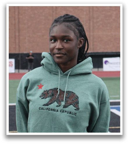 A young woman wearing a green hoodie stands in front of a football field. Contenido generado con IA